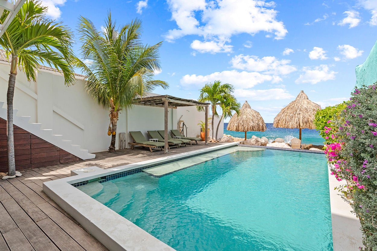 The private pool of the 5 Star Ocean Oasis with palm trees, palapas and the Caribbean Sea behind it