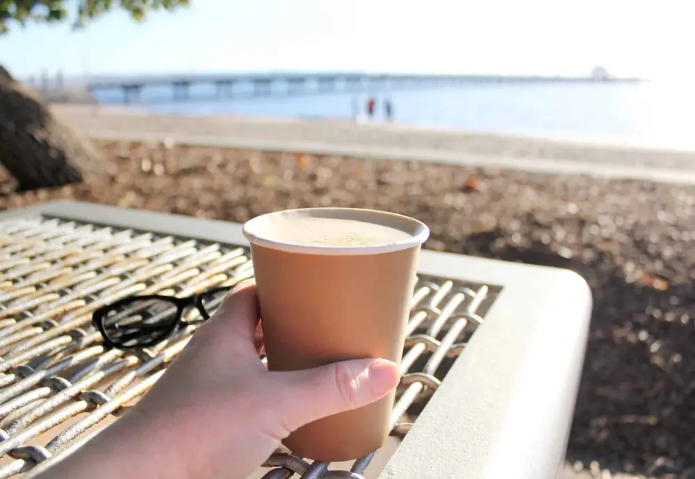 Een kop koffie in de hand met de zee op de achtergrond
