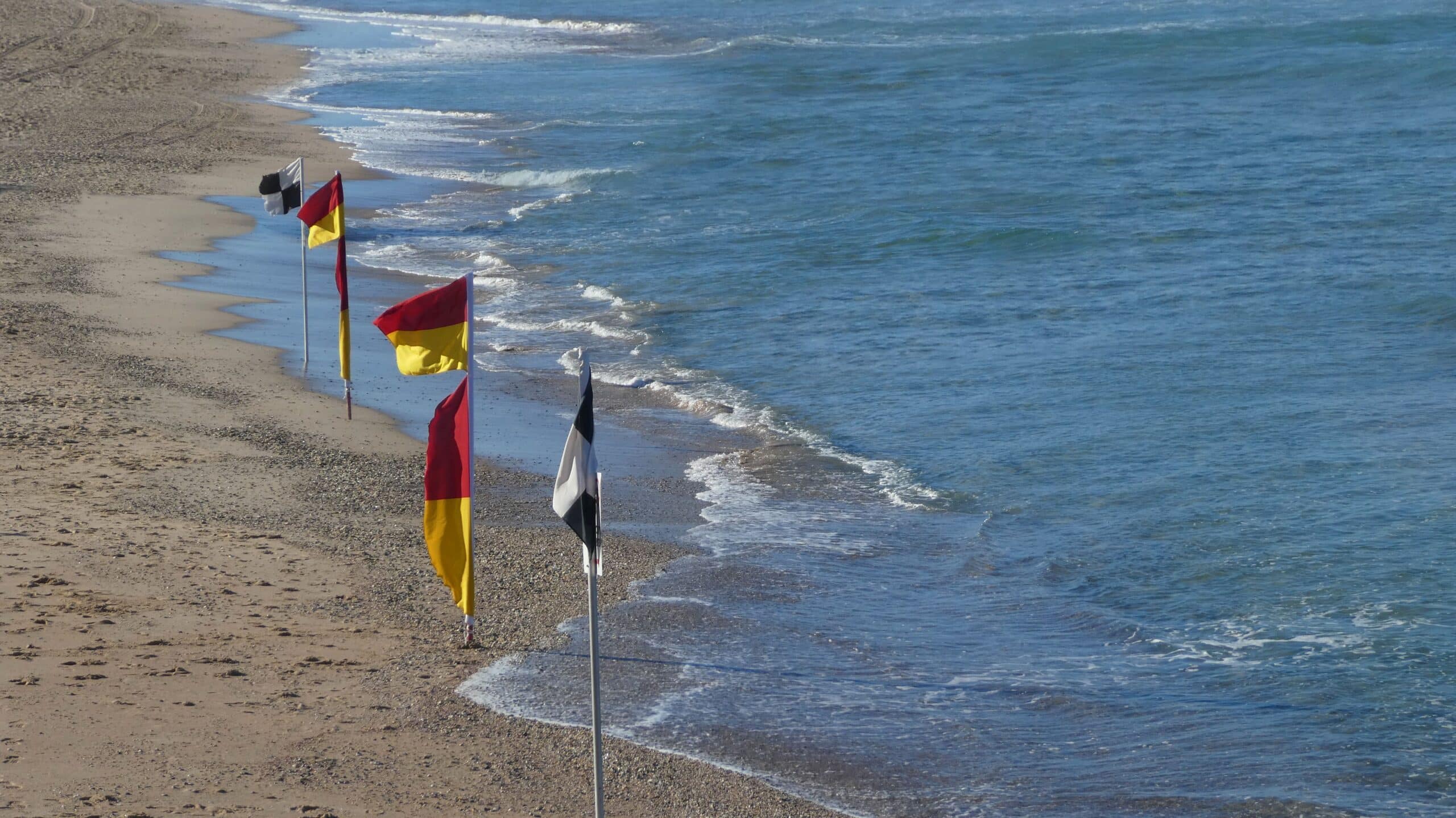 red and yellow beach flags including black and white flags along shoreline outdoors at the beach