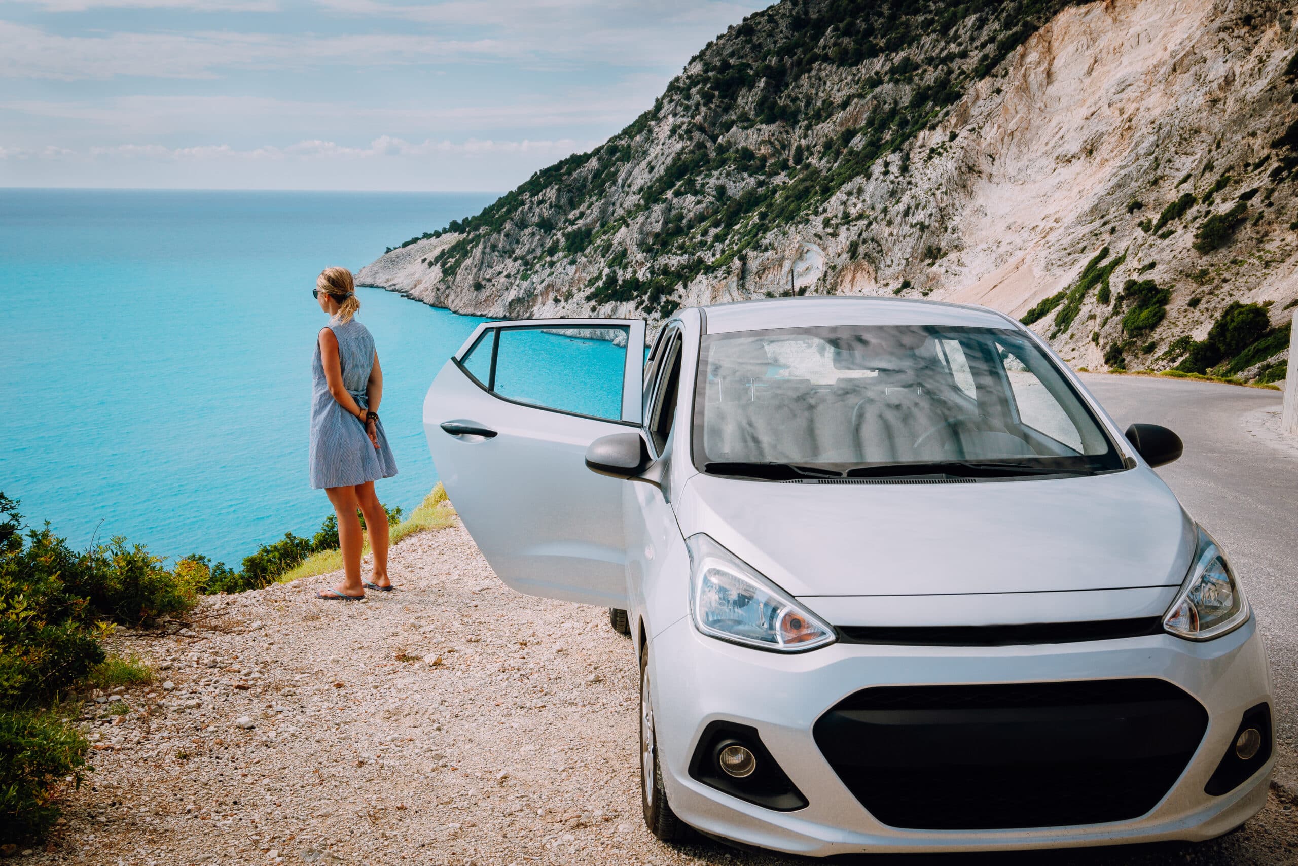 Women near rented car with open door enjoying Myrtos Beach. Travel vocation concept. Kefalonia, Ionian Sea, Greece.